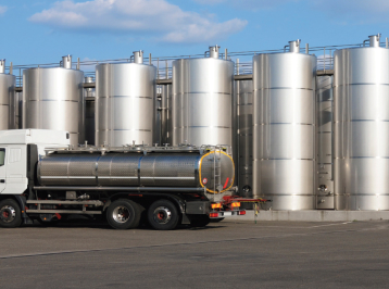 A large fuel truck next to fuel silos